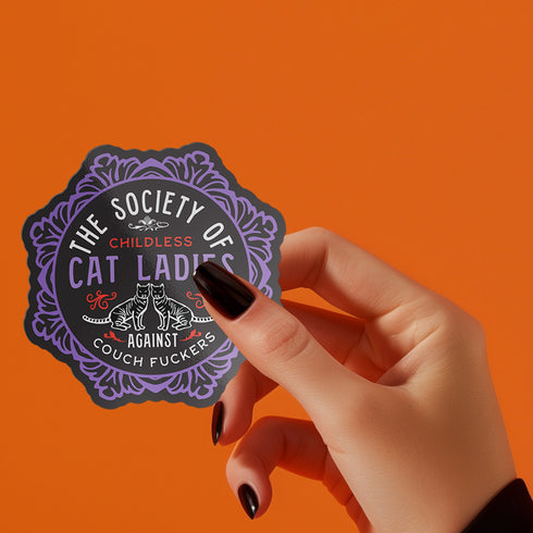 Round sticker with ornate border showing two cats and text "The Society of Childless Cat Ladies Against Couch Fuckers" in pink and purple versions on black background.